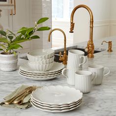 a kitchen counter with white dishes and gold faucets on it, next to a sink