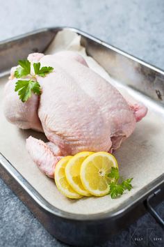 raw chicken with lemons and parsley in a metal pan on a counter top