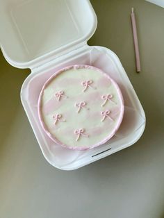 a cake in a plastic container with pink icing and bows on the top, next to a pencil