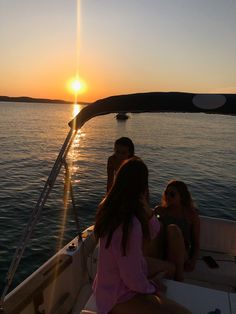 three people sitting on the back of a boat at sunset