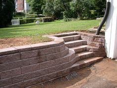 a brick wall with steps leading up to the front door and back yard area in the background