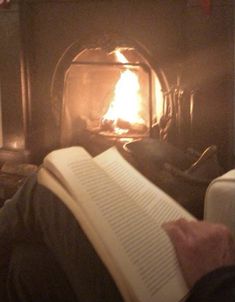 a person is reading a book in front of a fireplace with a lit candle on it