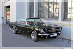 an old black mustang parked in front of a building