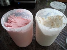 two plastic cups filled with ice cream sitting on top of a counter next to a blender