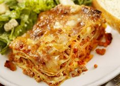 a white plate topped with lasagna next to a pile of salad and bread