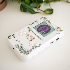 a white electronic device sitting on top of a table next to a flowery plant