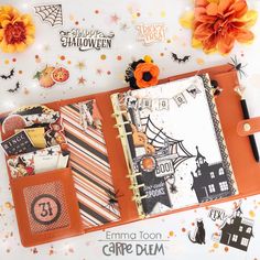 an open halloween planner book on a table with decorations and paper pumpkins in the background