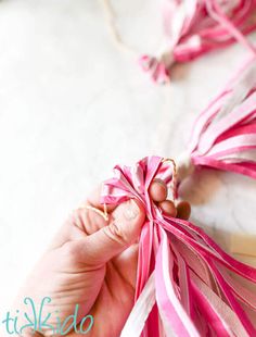 a person holding a piece of pink ribbon in their left hand and string attached to it