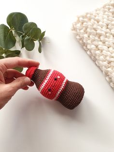 a hand holding a crocheted stuffed animal on top of a white table next to a plant