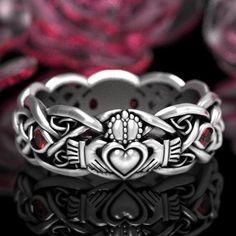 a silver ring with red stones in the center and hearts on it's sides