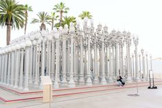 a person sitting on a bench in front of a row of white street lamps and palm trees