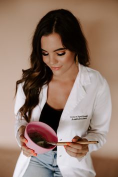 a woman in a white lab coat holding a pink bowl and spoon with chopsticks