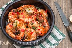 a bowl filled with cooked shrimp and garnished with herbs next to a slice of bread