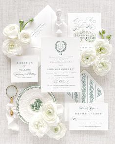 the wedding stationery is laid out with white flowers and greenery on top of it