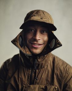 a man in a brown jacket and hat smiling at the camera with his hood up