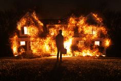 a man standing in front of a house on fire with his handbag and briefcase