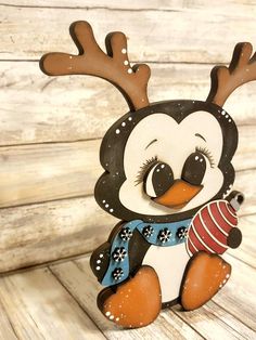 a wooden penguin with antlers on its head holding a christmas ornament in it's paws