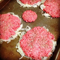 four hamburger patties cooking in a pan with onions and seasoning on top, ready to be cooked