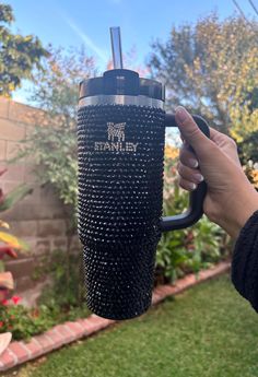 a person holding a black coffee cup in their hand with the words stanley on it