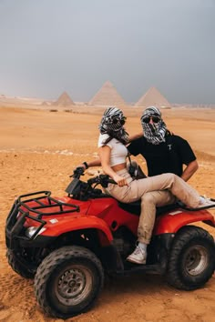 two people are riding an atv in the desert with pyramids in the back ground