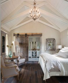 a white bedroom with wood floors and a chandelier hanging from the vaulted ceiling