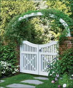 a white gate surrounded by flowers and greenery