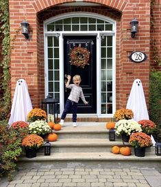 a little boy standing on the steps outside of a house decorated for halloween with decorations and pumpkins