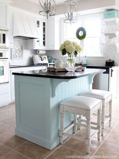 a kitchen with white cabinets and light blue island in the center, surrounded by two stools