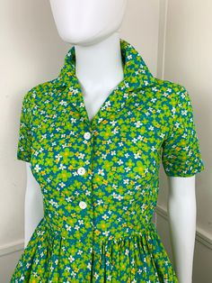 Cheerful 1960's daisy print shirtwaist dress. Teal cotton blend with a lime green, white and marigold all over daisy print. It's just darling! Classic shirtwaist silhouette with a collared neck and short sleeves. Small white plastic daisy buttons down the front. Metal snap and hook and eye secures the waisy. Full skirt. Opaque and unlined. { LABEL- FABRIC- TAG SIZE }No labels. It appears home sewn.Cotton BlendNo size tags{ MEASUREMENTS }Shown on a 5'8" Mannequin with 33" Bust- 25" Waist- 35" Hips All measurements taken FLAT and doubled Bust- 34" Measurement taken arm pit to arm pit Waist- 27"Hips- up to 72"Total Length- 38" with 3" of seam allowance{ CONDITION }Excellent Condition: A few loose threads at the waist. Shown in last photo. Short Sleeve Cotton Dress With Retro Print, Cotton Short Sleeve Dresses With Retro Print, Cotton Dresses With Retro Print And Short Sleeves, Green Collared Cotton Dress, Green Cotton Collared Dress, Vintage Green Collared Dress, Toad And Co, Green Daisy, Seam Allowance