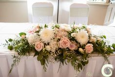 an arrangement of flowers on a table with white chairs in the background at a wedding reception