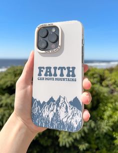 a person holding up a phone case with the words faith on it and mountains in the background