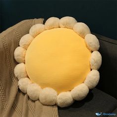 a yellow pillow with white pom - poms is on top of a chair