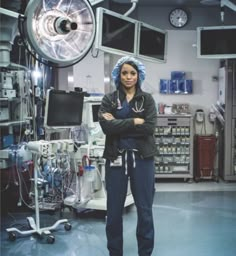 a woman in scrubs stands with her arms crossed and looks at the camera, surrounded by medical equipment