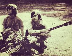 two young men sitting on the ground with flowers and an electric guitar in front of them