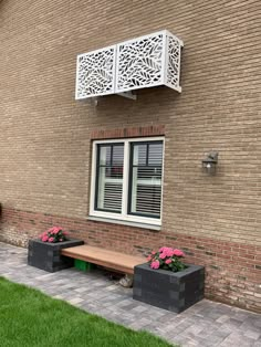 a brick building with two benches in front of it and pink flowers on the lawn