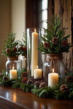 candles are lit on a mantle with evergreen branches and pine cones in glass vases