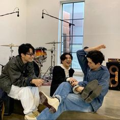 three young men sitting on the floor in front of musical instruments, one holding his leg up