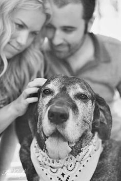 a man and woman are petting a dog's head with a bandana around its neck