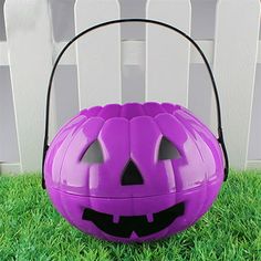 a purple pumpkin shaped basket sitting on top of green grass next to a white fence