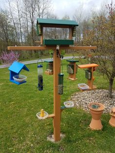 a bird feeder in the middle of a grassy area with two toilets and several birds