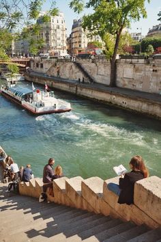 people are sitting on the steps looking at boats going down the river in front of them