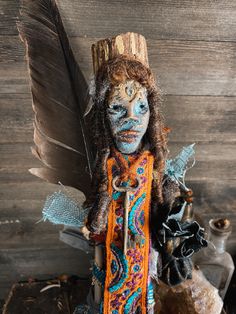 a doll with painted face and feathers on it's head, standing next to a wooden