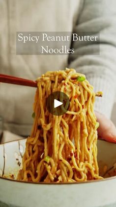 a person holding chopsticks over noodles in a bowl with the caption spicy peanut butter noodles