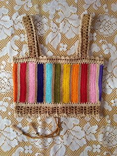 a crocheted bag with multicolored handles on a lace doily background