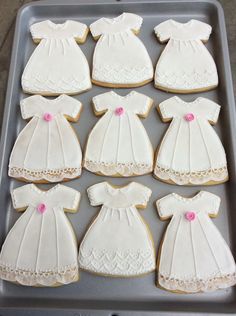 decorated cookies in the shape of baby's gowns on a baking sheet with pink buttons