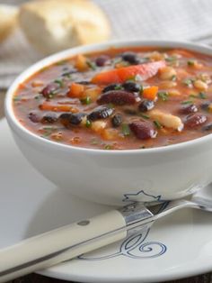 a white bowl filled with beans and carrots on top of a plate next to bread