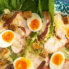 a salad with hard boiled eggs, bacon and lettuce in it on a blue plate