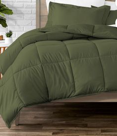 a bed with green comforter and pillows in a room next to a white brick wall