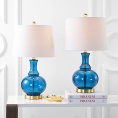 two blue glass lamps sitting on top of a table next to a white lamp shade