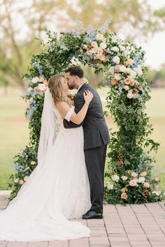 a bride and groom kissing in front of an arch with flowers on it at their wedding